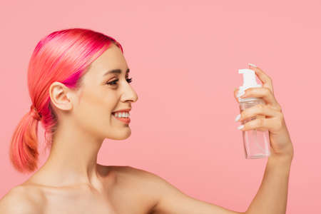 happy young woman with colorful hair looking at bottle with toner isolated on pinkの写真素材