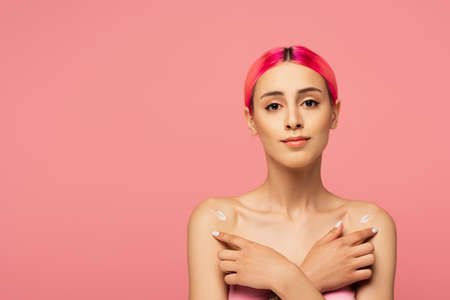 young woman with colorful hair applying lotion on bare shoulders isolated on pinkの写真素材