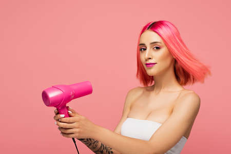 pretty young woman with colorful hair holding hair dryer isolated on pinkの写真素材