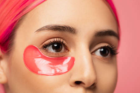 partial view of young woman with dyed hair and collagen eye patch isolated on pink