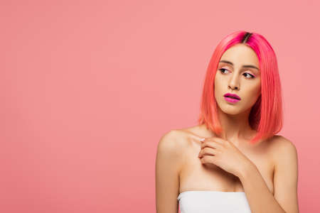 young woman with colorful hair and bright makeup looking away isolated on pinkの写真素材