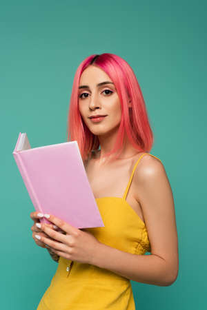pretty young woman with pink dyed hair holding book isolated on blue