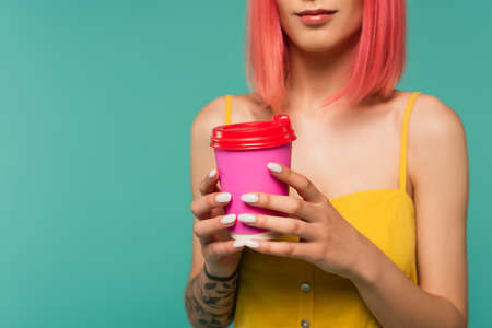 cropped view of young woman with pink dyed hair holding paper cup isolated on blueの写真素材