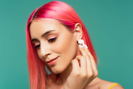 young woman with pink dyed hair holding wireless earphone isolated on blue