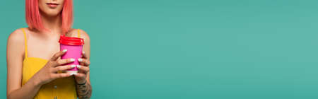 cropped view of young woman with pink dyed hair holding paper cup isolated on blue, bannerの写真素材