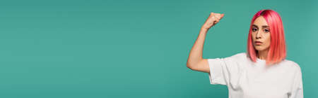 strong young woman with pink dyed hair showing muscle isolated on blue, bannerの写真素材