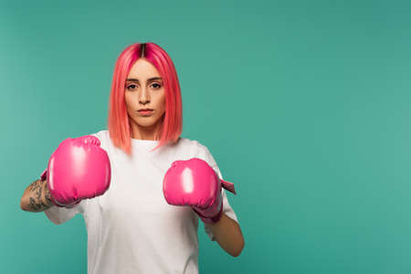 tattooed young woman with pink dyed hair in boxing gloves isolated on blueの写真素材