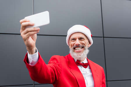 happy mature man in santa hat taking selfie near grey wallの写真素材