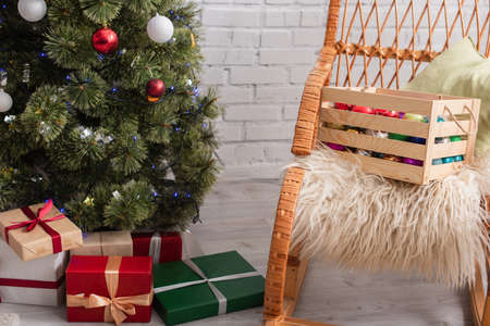 wooden box with decorative baubles on wicker chair near presents under christmas treeの写真素材