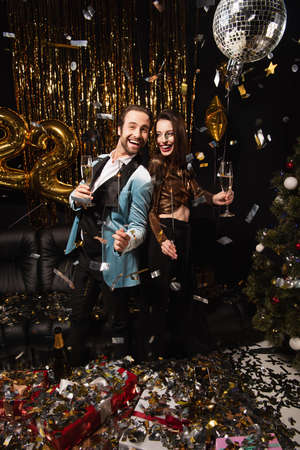 cheerful and elegant couple with sparklers celebrating christmas near shiny decoration on blackの写真素材