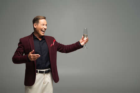 Positive man in formal wear pointing at glass of champagne isolated on grey