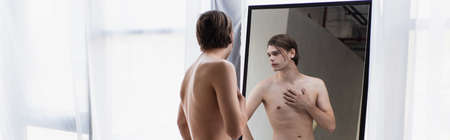 shirtless transgender young man looking at mirror, banner
