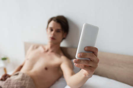 blurred and shirtless transgender man taking selfie on smartphoneの写真素材