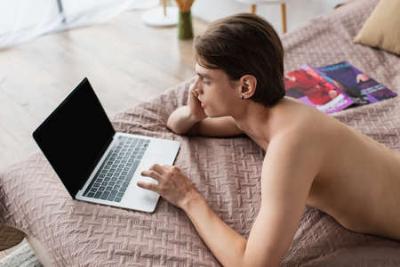 high angle view of shirtless transgender man using laptop with blank screen on bed