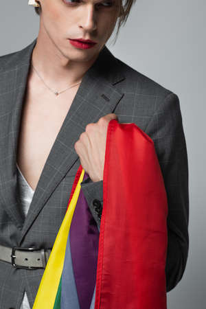 young transsexual man in blazer holding lgbt flag isolated on greyの写真素材