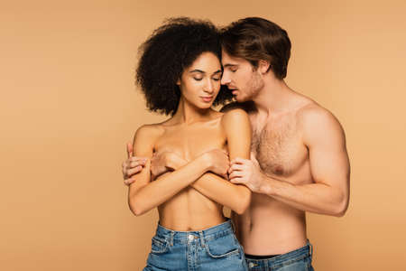 sexy man hugging topless hispanic woman covering breast with crossed arms isolated on beigeの写真素材