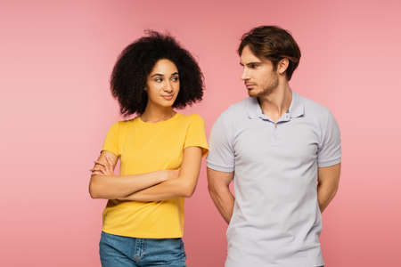 positive latin woman and offended man looking at each other isolated on pinkの写真素材