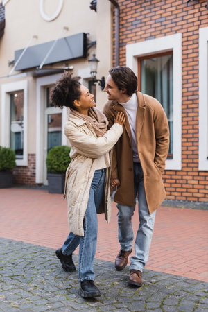 full length of cheerful african american woman holding hands while standing with boyfriend outdoorsの写真素材