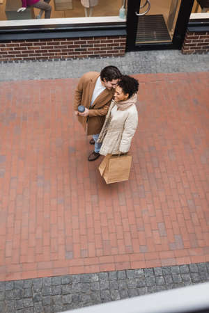 top view of joyful man holding paper cup near pleased african american girlfriend with purchases in mallの写真素材