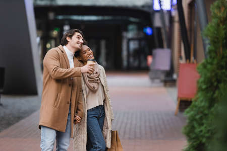 african american woman holding shopping bags near happy boyfriend in coat in mallの写真素材