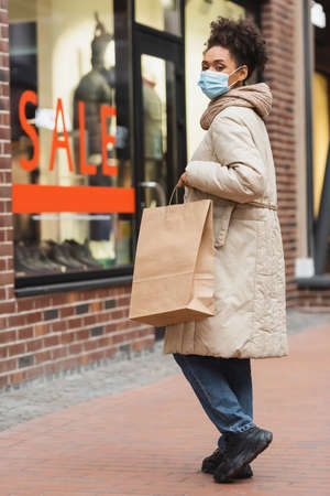 brunette african american woman in medical mask doing christmas shopping in mallの写真素材