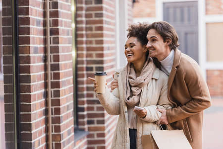 happy african american woman with paper cup pointing at building near boyfriendの写真素材