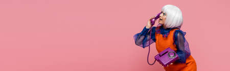 Side view of cheerful asian pop art model talking on telephone isolated on pink, bannerの写真素材