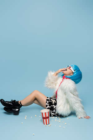 Stylish asian pop art woman in 3d glasses eating popcorn on blue background