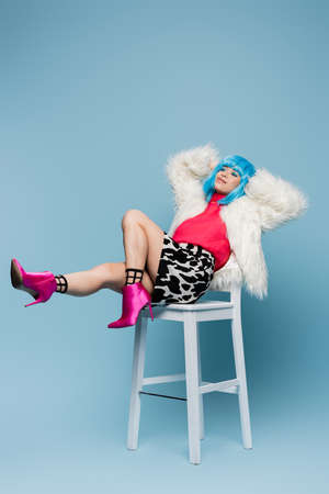 Smiling asian woman in pop art style sitting on white chair on blue backgroundの写真素材