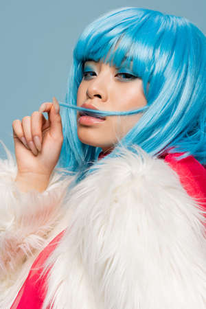 Portrait of stylish asian woman touching hair isolated on blueの写真素材