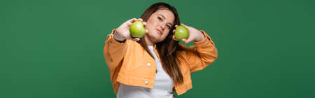 Pretty woman with overweight holding green apples isolated on green, bannerの写真素材