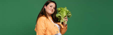 Smiling woman with overweight holding lettuce and looking at camera isolated on green, banner