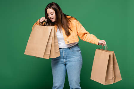 Amazed woman with overweight looking at shopping bags isolated on greenの写真素材