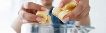 Cropped view of blurred woman holding banana slices near blender, bannerの写真素材