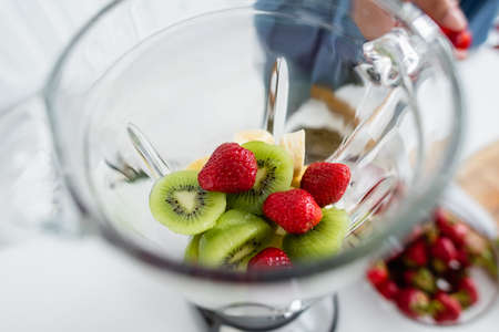 Cropped view of fresh fruits in blender near blurred woman in kitchenの写真素材