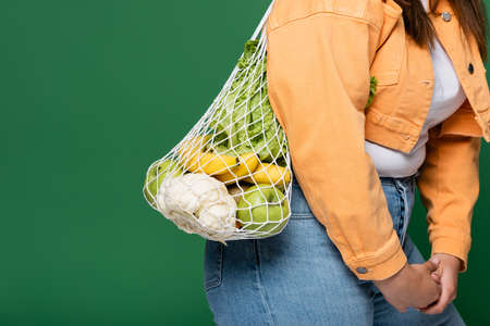 Cropped view of woman with overweight with net bag and fresh food isolated on greenの写真素材