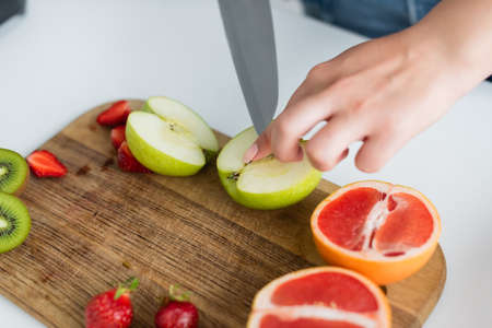 Cropped view of woman cutting apple near grapefruit and strawberries on cutting boardの写真素材