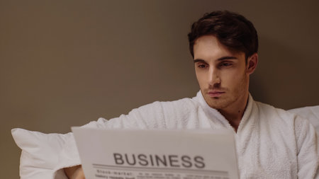 focused man reading business newspaper while resting in hotel roomの写真素材