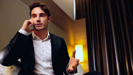 businessman gesturing while talking on cellphone in hotel room
