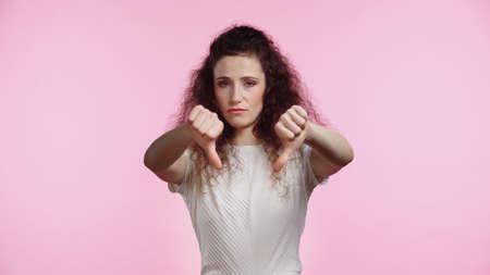 displeased young woman showing thumbs down isolated on pinkの写真素材