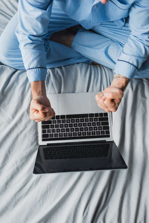 Top view of freelancer in pajama showing yes gesture near laptop on bedの写真素材