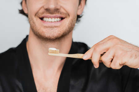 Cropped view of smiling man in robe holding toothbrush isolated on greyの写真素材