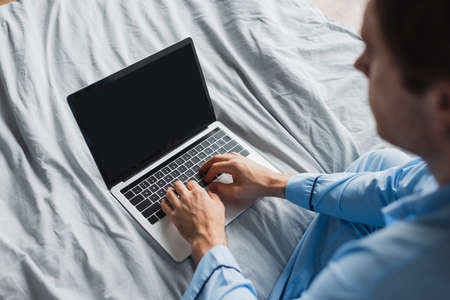 High angle view of blurred man in pajama using laptop with blank screen on bedの写真素材