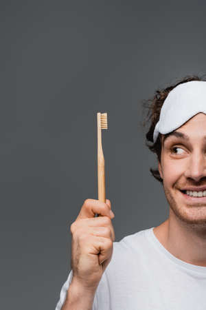 Cropped view of smiling man in sleep mask looking at toothbrush isolated on greyの写真素材