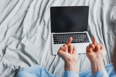 Cropped view of freelancer in pajama showing middle fingers at laptop on bedの写真素材