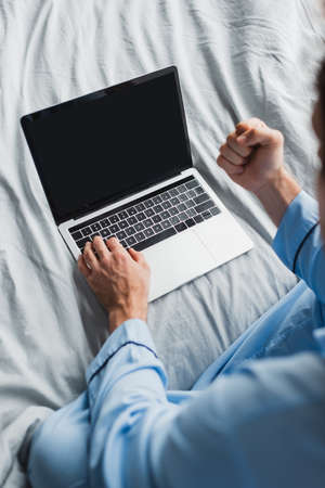 Top view of blurred freelancer in pajama showing yes gesture while using laptop on bedの写真素材
