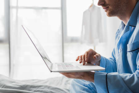 Cropped view of young man in pajama using laptop on bed in morningの写真素材