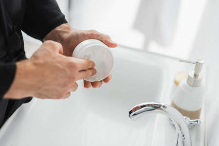 Cropped view of man taking cosmetic cream from container near sink in bathroomの写真素材