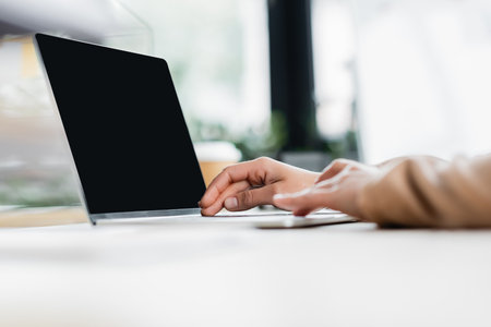 cropped view of businesswoman typing on laptop with blank screen in office on blurred foregroundの写真素材