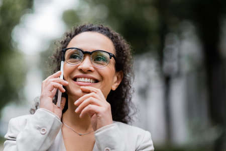 happy african american businesswoman in eyeglasses talking on mobile phone outdoorsの写真素材